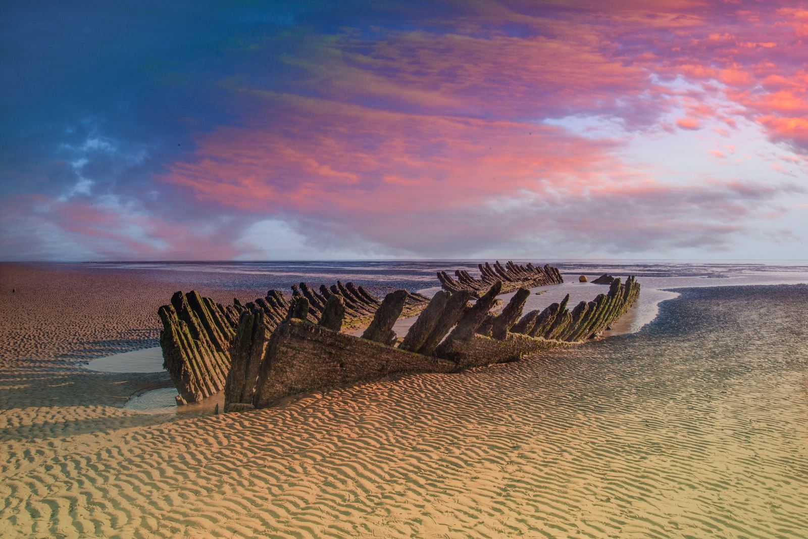 The carcass of a shipwreck stuck in the sand at sunset 